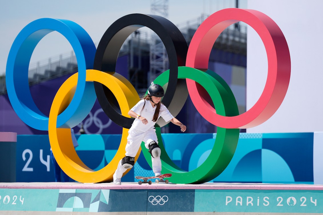 Fay De Fazio Ebert sur son skateboard devant les anneaux olympiques.