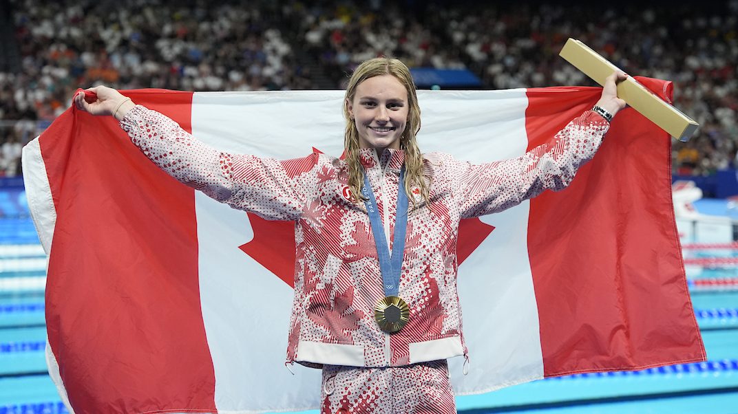 Summer McIntosh pose avec sa médaille d'or et le drapeau canadien.