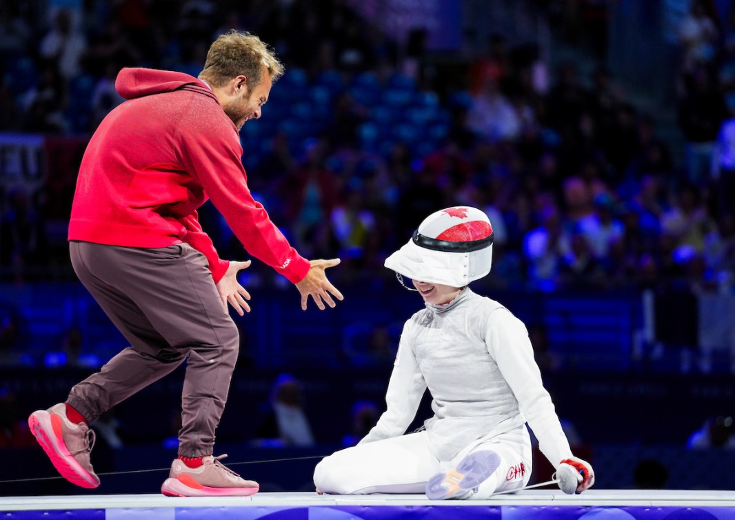 Eleanor Harvey est assise sur la piste d'athlétisme, son entraîneur vient la rejoindre en souriant. 