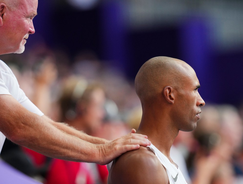 Damian Warner de profil, son entraîneur a les mains sur ses épaules.