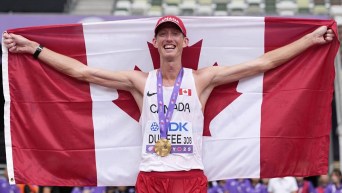 Evan Dunfee tient le drapeau canadien derrière lui, une médaille d’or autour du cou sur son maillot blanc