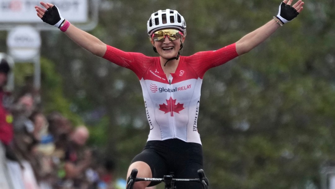 Magdeleine Vallières, vêtue de sa tenue de cyclisme sur route rouge et blanche, lève les bras en signe de victoire.