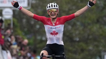 Magdeleine Vallières, vêtue de sa tenue de cyclisme sur route rouge et blanche, lève les bras en signe de victoire.