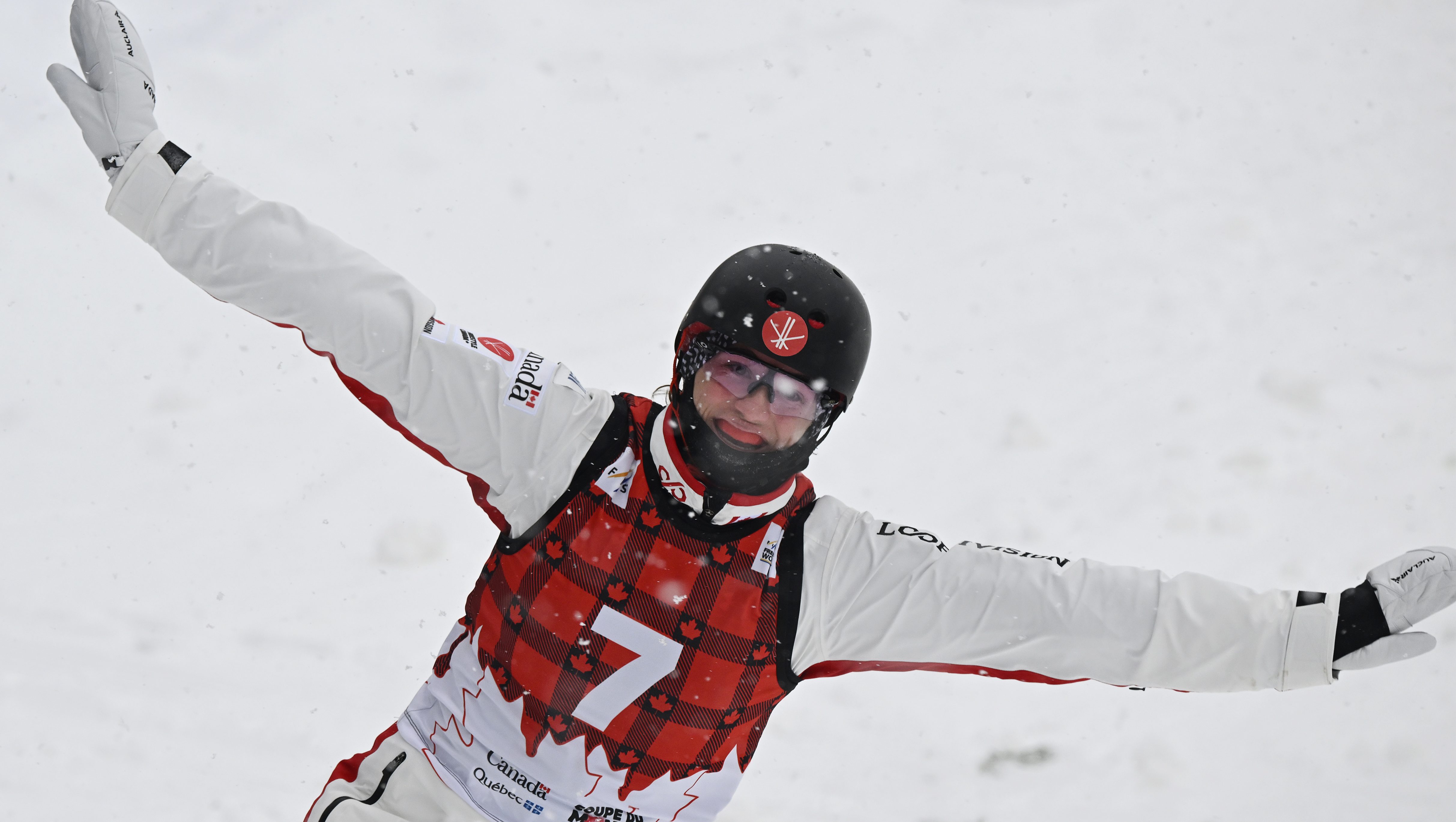 Wearing a red plaid bib over a white snowsuit, Marion Thenault smiles after landing a jump