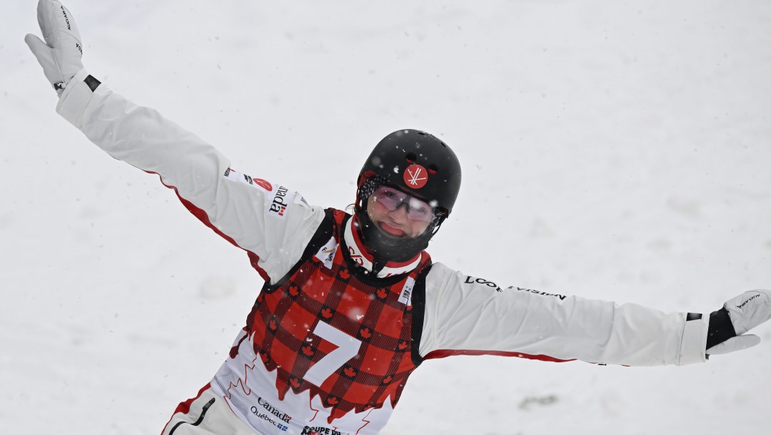 Wearing a red plaid bib over a white snowsuit, Marion Thenault smiles after landing a jump