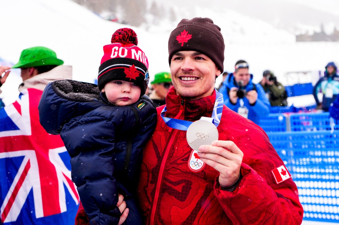 Mikaël Kingsbury tient son fils Henrik avec son bras droit, sa médaille d'argent dans la main gauche. 