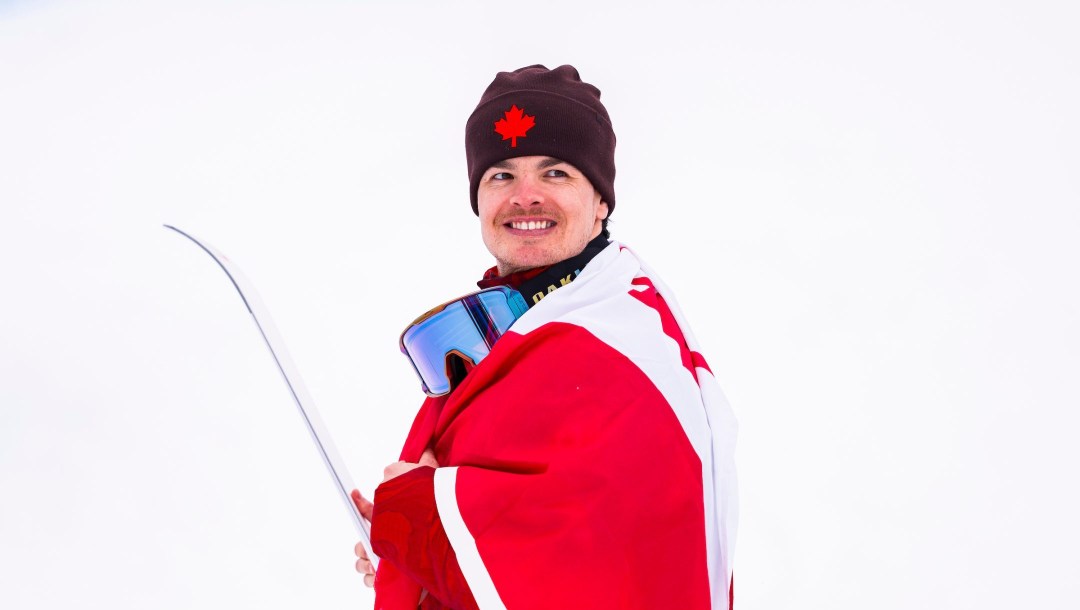 Mikaël Kingsbury sourit avec le drapeau du Canada sur les épaule.