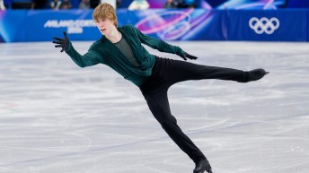 Stephen Gogolev, aux cheveux blonds et vêtu d'une chemise verte à manches longues et d'un pantalon noir, glisse en arrière sur un pied, en patins.